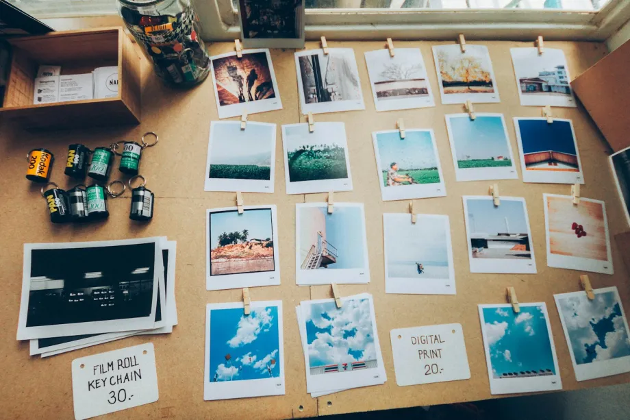 Assorted printed photographs spread across a beige wooden table