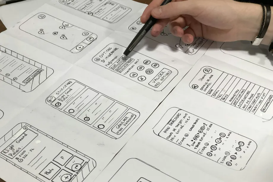 Hand holding a pen over paper wireframe sketches of a web page layout