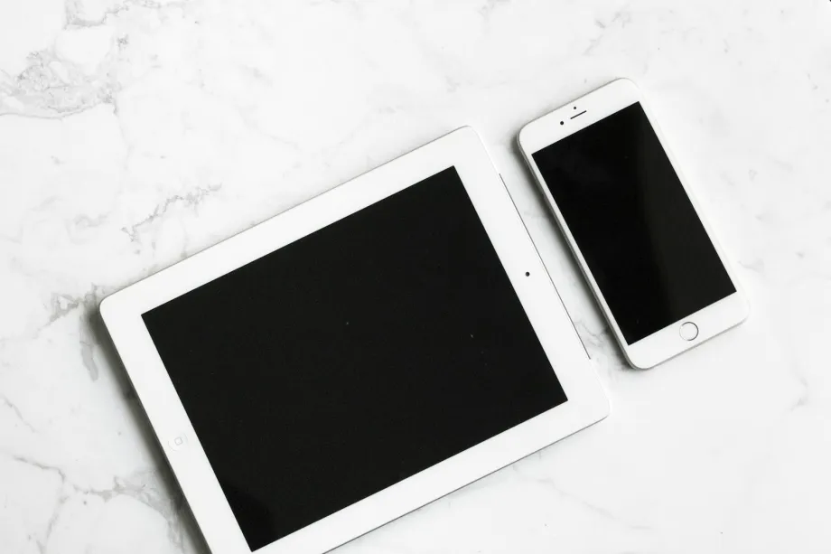 White tablet and silver smartphone lying side by side on a white surface